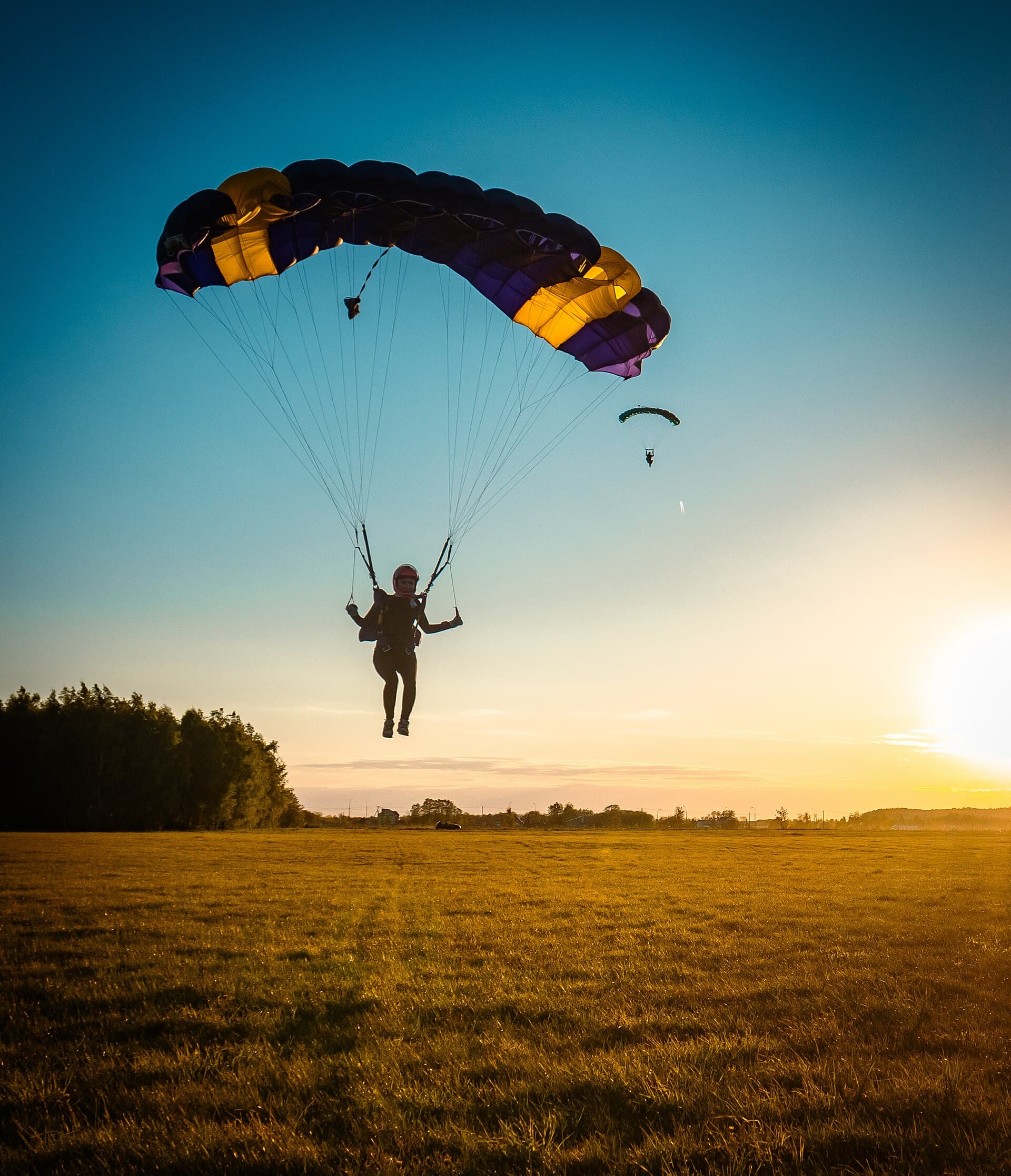 Tandem skydiver mid-freefall above a curved tropical coastline, reef visible through clear water, parachute just starting to deploy in the corner of the frame.