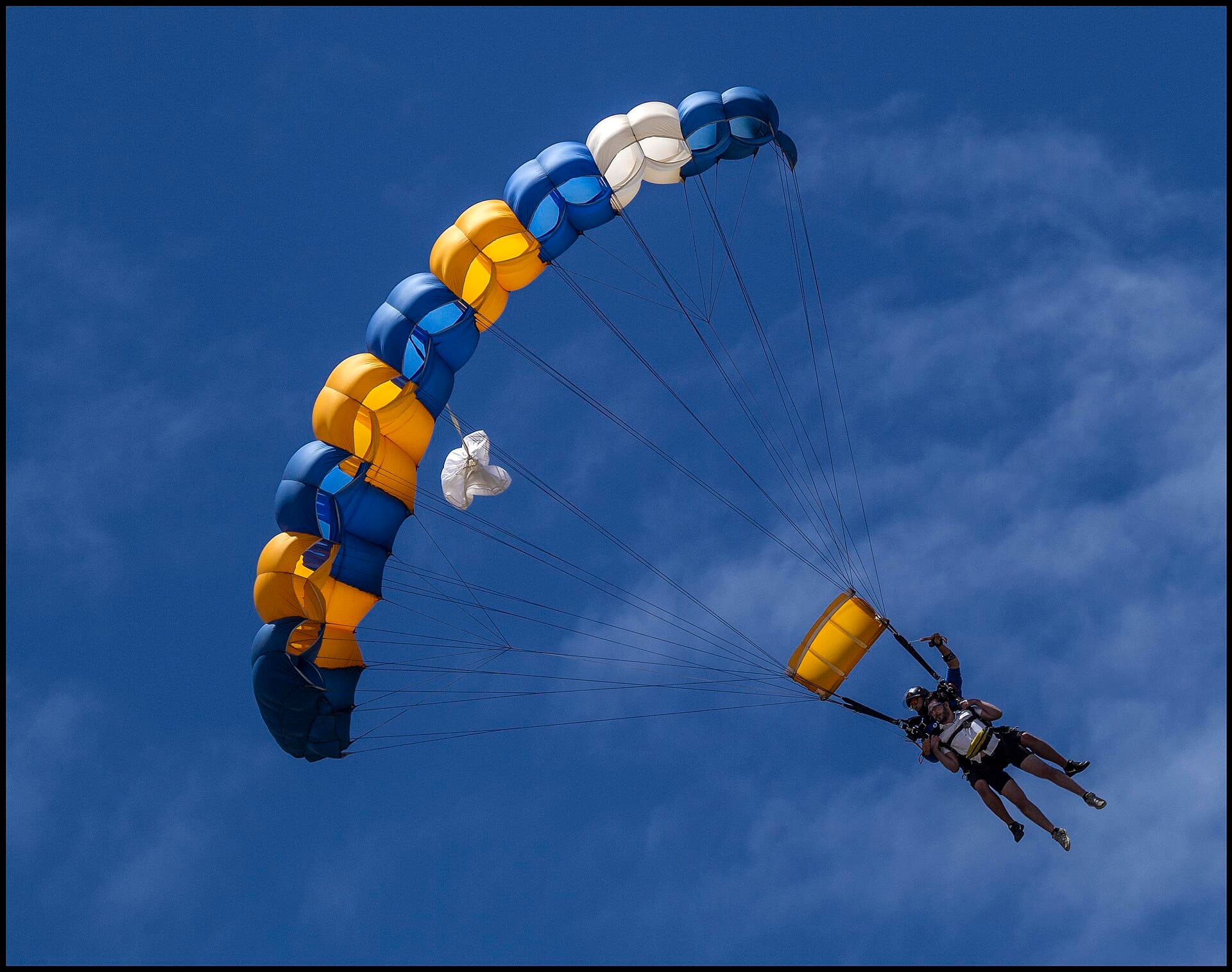 Tandem skydiver and instructor mid-freefall over Mission Beach, reef visible, rainforest coastline below, student grinning. GoPro-style frame without feeling stock.